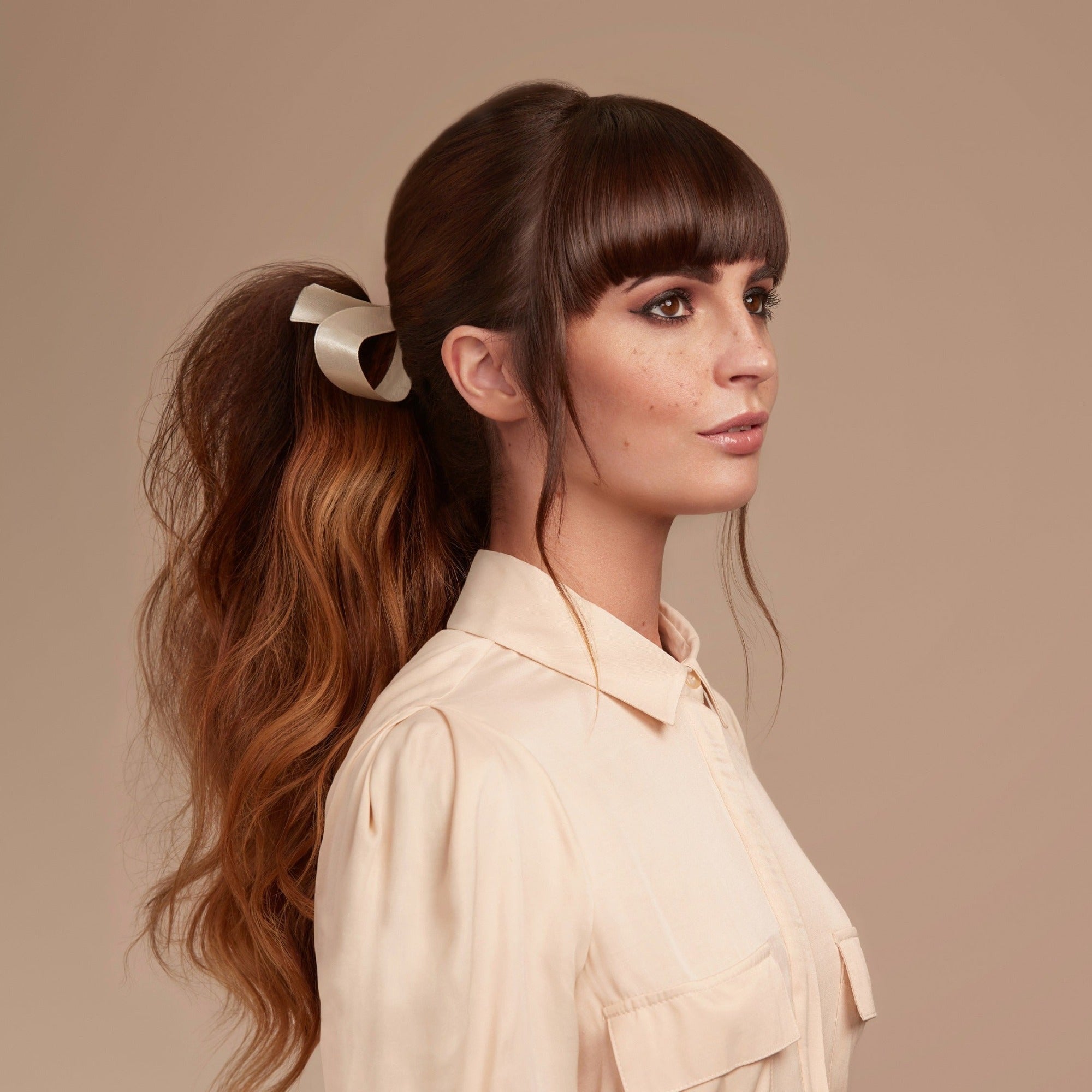 Female model with long wavy brunette hair tied into a low pony tail with a cream ribbon.  Her hair is very shiny from using Moo and Yoo Miracle Conditioner and full of volume form Moo and Yoo Volumising Spray Mist. She is wearing a cream shirt.