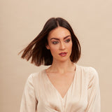 Female model with a super straight brunette bob. She has super shiny hair from using Moo and Yoo conditioner. She is looking at the camera and is wearing a neutral coloured blouse.