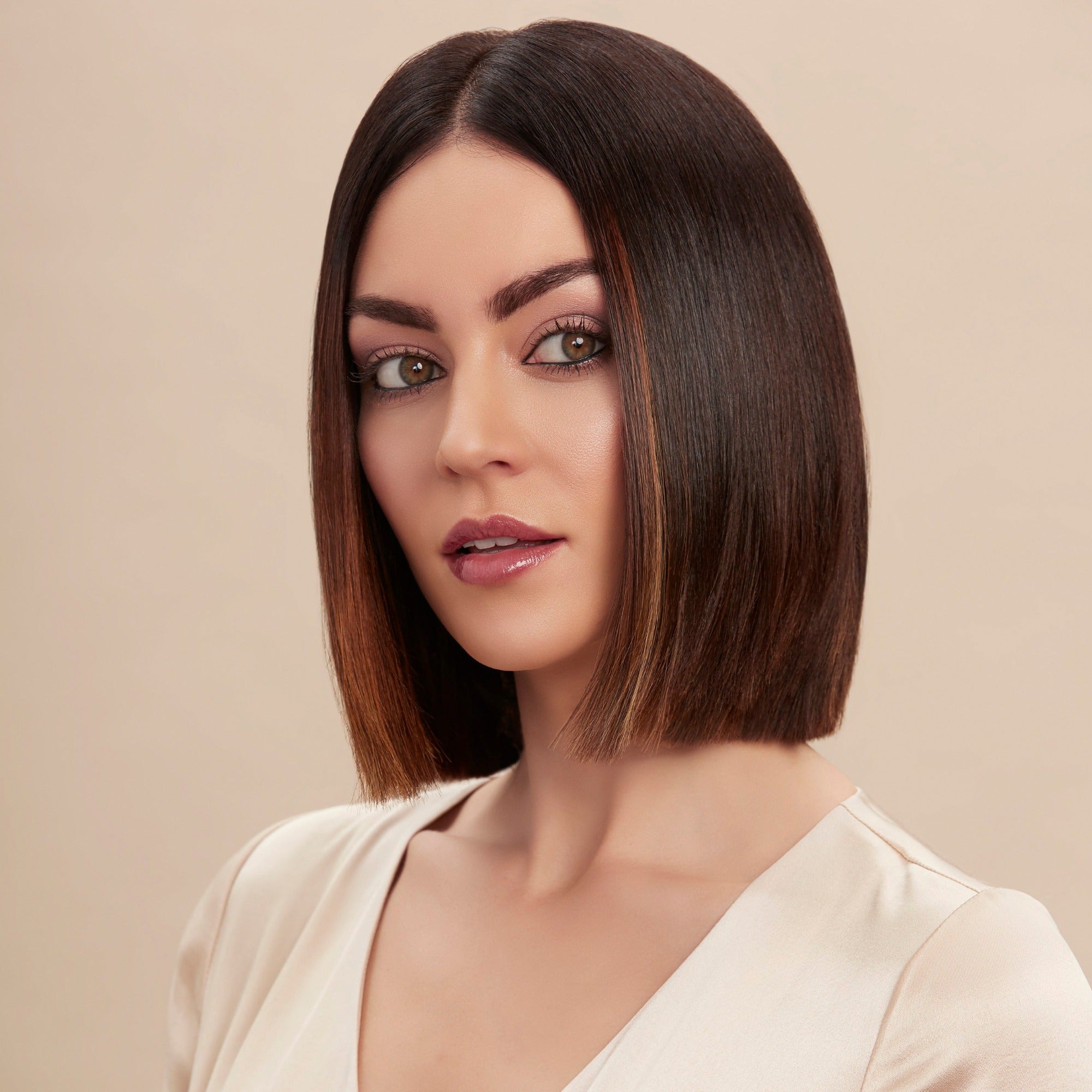 Female model with a super straight brunette bob from using Moo and Yoo Miracle Conditioner and every hair is kept in place by Moo and Yoo Hair Spray. She has super shiny hair. She is looking at the camera and is wearing a neutral coloured blouse.