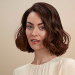 Female model with a wavy bob and brunette hair. She has super shiny hair and has used Moo & Yoo Miracle Conditioner and Volumising Spray Mist so she has  lots of volume. She is looking at the camera from a side angle and is wearing a neutral coloured top.