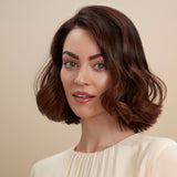 Female model with a wavy bob and brunette hair. She has super shiny hair and has used Moo & Yoo Miracle Shampoo, Conditioner, Miracle Milk and Volumising Spray Mist so her hair has lots of volume. She is looking at the camera from a side angle and is wearing a neutral coloured shirt.