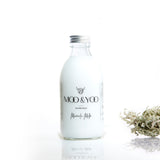 A glass bottle of Moo and Yoo Miracle Milk with an aluminium lid on a white background with a sprig of Icelandic moss placed to one side.