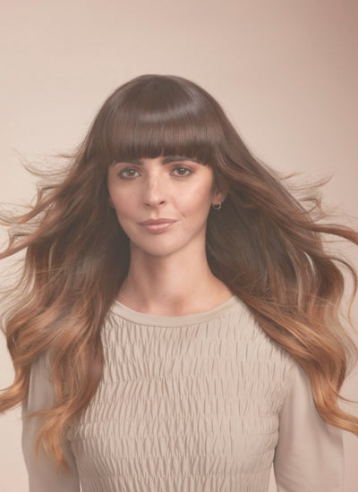 girl with long flowing brunette hair flowing in the wind with a sleek shiny straight fringe facing the camera directly. Natural skin and freckles 