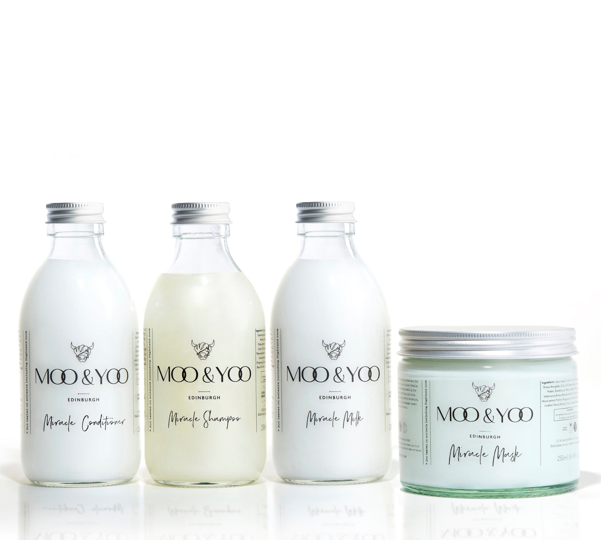 Three glass bottles and a glass jar of Moo and Yoo products sitting side by side. It is a Miracle Shampoo, Conditioner, Miracle Milk and a Miracle mask. They all have aluminium lids.  They are on a white background.