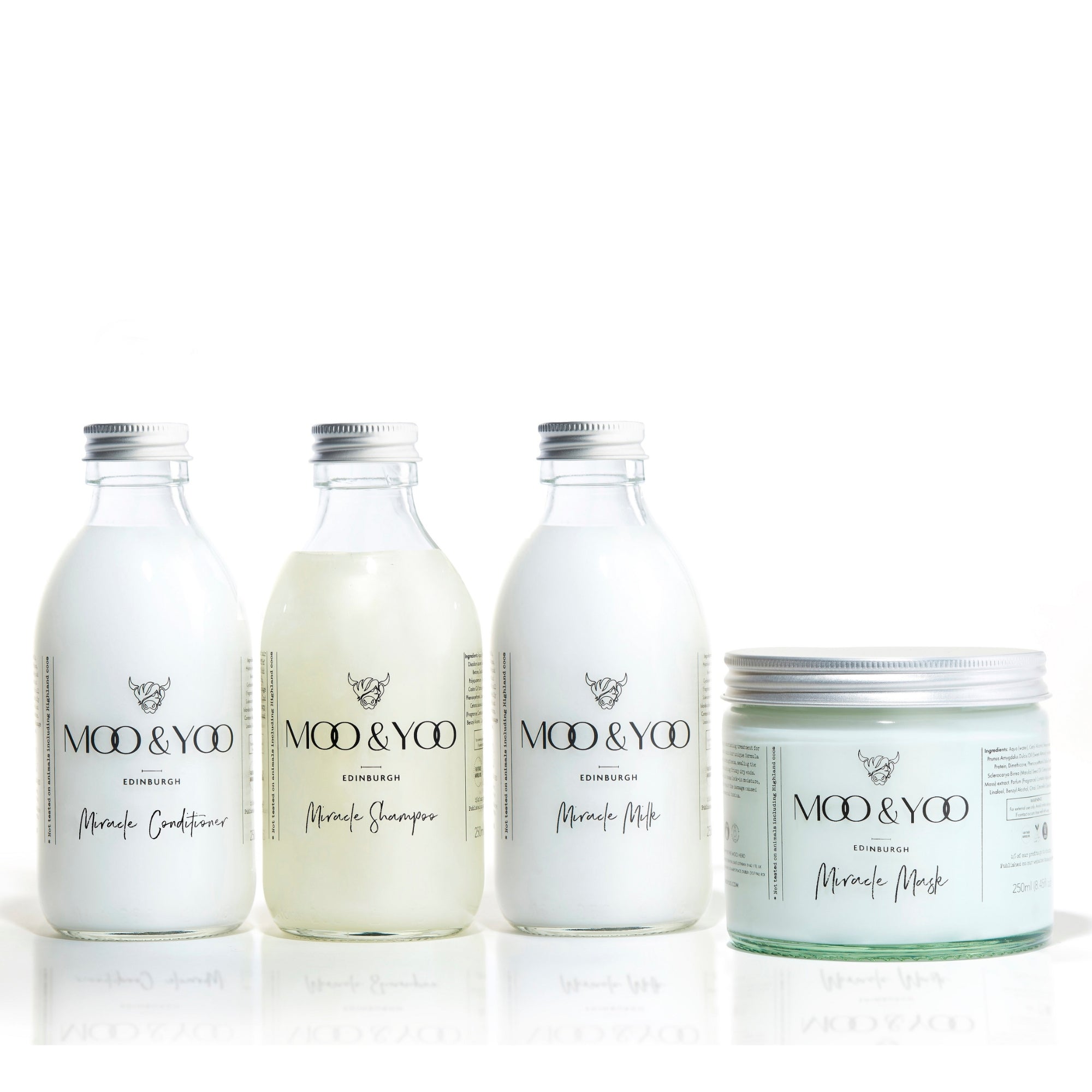 Three glass bottles and a glass jar of Moo and Yoo products sitting side by side. It is a Miracle Shampoo, Conditioner, Miracle Milk and a Miracle mask. They all have aluminium lids.  They are on a white background.
