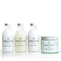 Three glass bottles and a glass jar of Moo and Yoo products sitting side by side. It is a Miracle Shampoo, Conditioner, Miracle Milk and a Miracle mask. They all have aluminium lids.  They are on a white background.