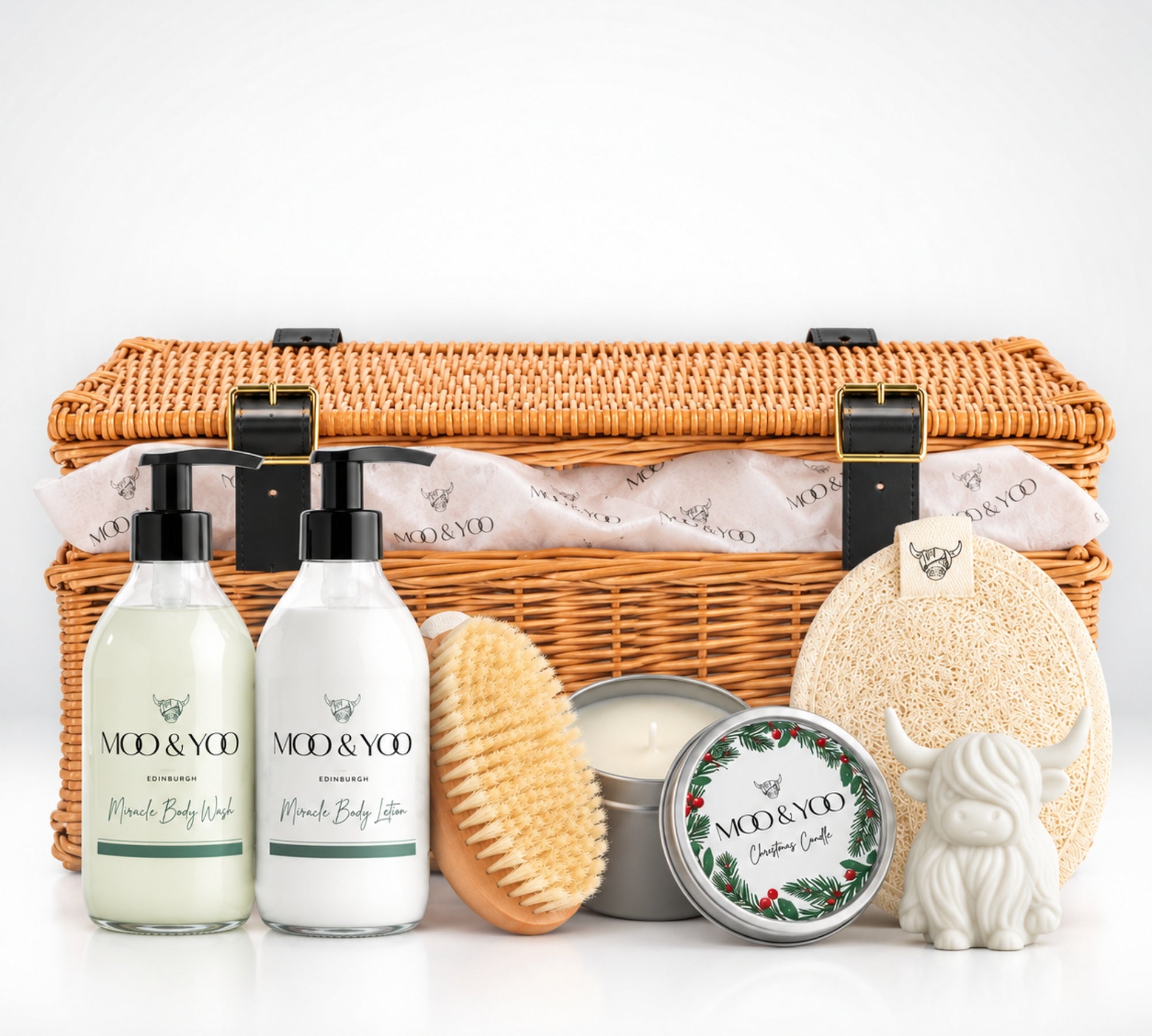 Moo & Yoo Luxury Body Care Christmas Hamper featuring Miracle Body Wash, Body Lotion, sisal body brush, body buffer, Highland cow soap and festive candle in a wicker basket with branded tissue paper.