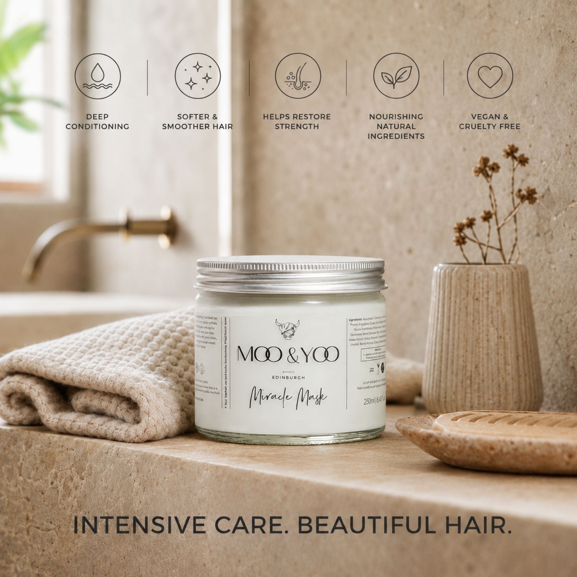 A jar of MOO & YOO Miracle Mask hair treatment sits on a stone countertop in a bathroom setting, styled with a beige towel, a small vase of dried flowers, and a wooden dish. Above the product, five feature icons with text describe deep conditioning, softer and smoother hair, helps restore strength, nourishing natural ingredients, and vegan and cruelty free.