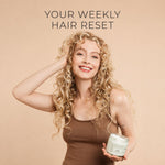 A smiling woman with long curly blonde hair holds a jar of moo and yoo miracle mask hair product against a warm beige background, with the text 'YOUR WEEKLY HAIR RESET' above her.