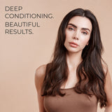 A woman with long, dark brown wavy hair wearing a brown top, posed against a solid beige background with the text 'DEEP CONDITIONING. BEAUTIFUL RESULTS.