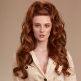 Woman with long, wavy red hair wearing a light-colored blouse against a beige background