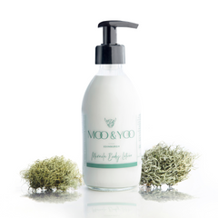 Glass bottle of Miracle Body Lotion with a pump on a white background with a sprig of moss on each side.