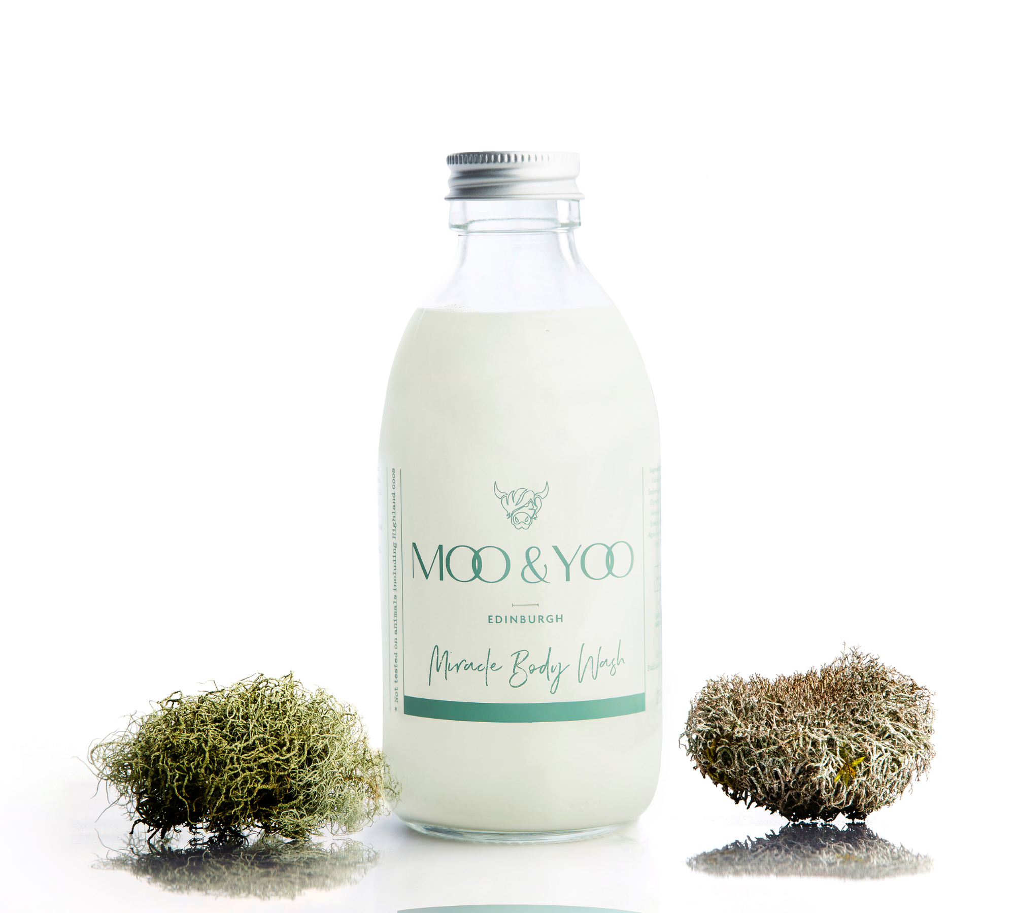 Glass bottle of Miracle Body Wash with an aluminium lid on a white background with a sprig of moss on each side.