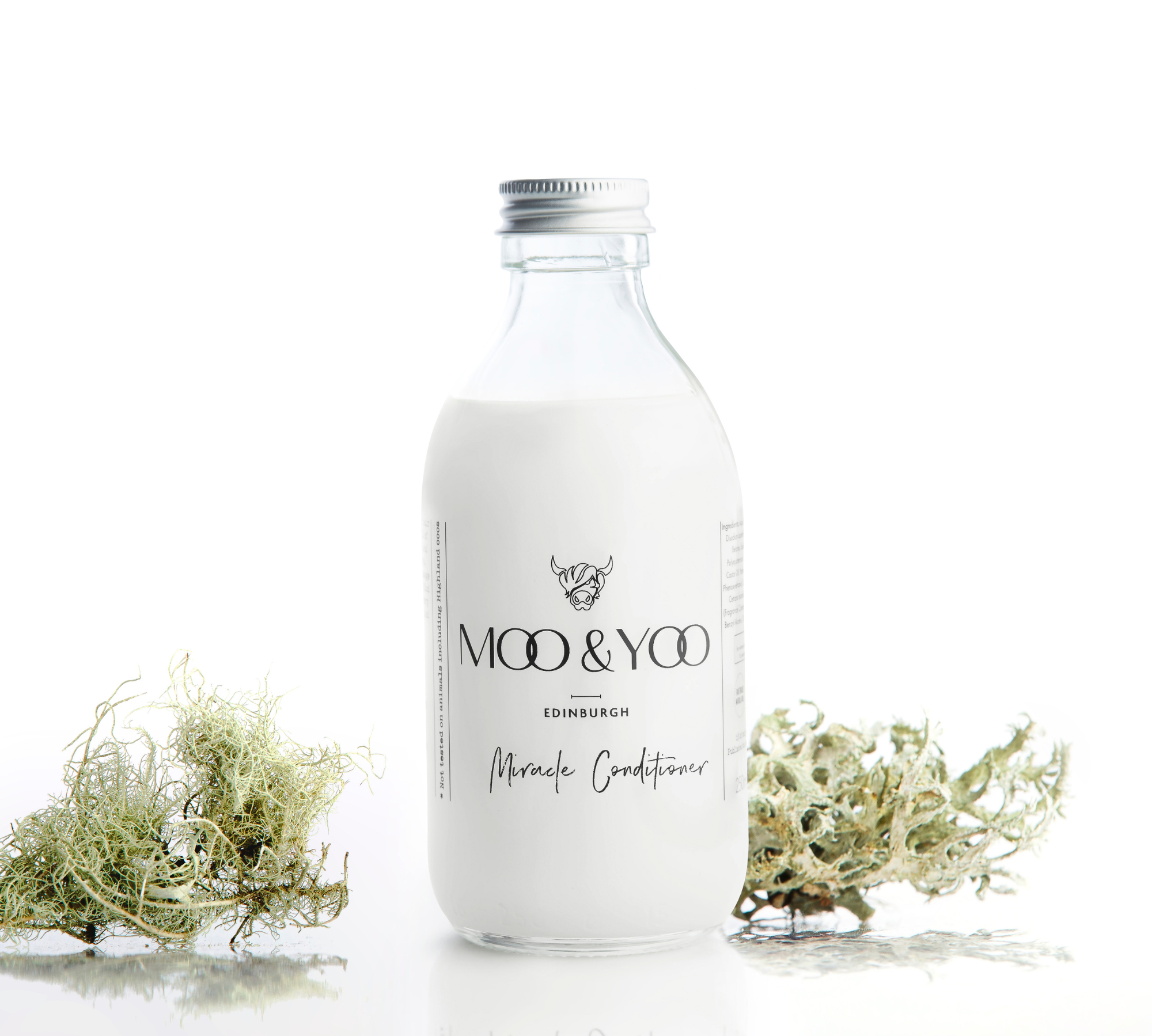 A glass bottle of Moo and Yoo Miracle conditioner with an aluminium lid on a white background with a sprig of Icelandic moss placed to each side.