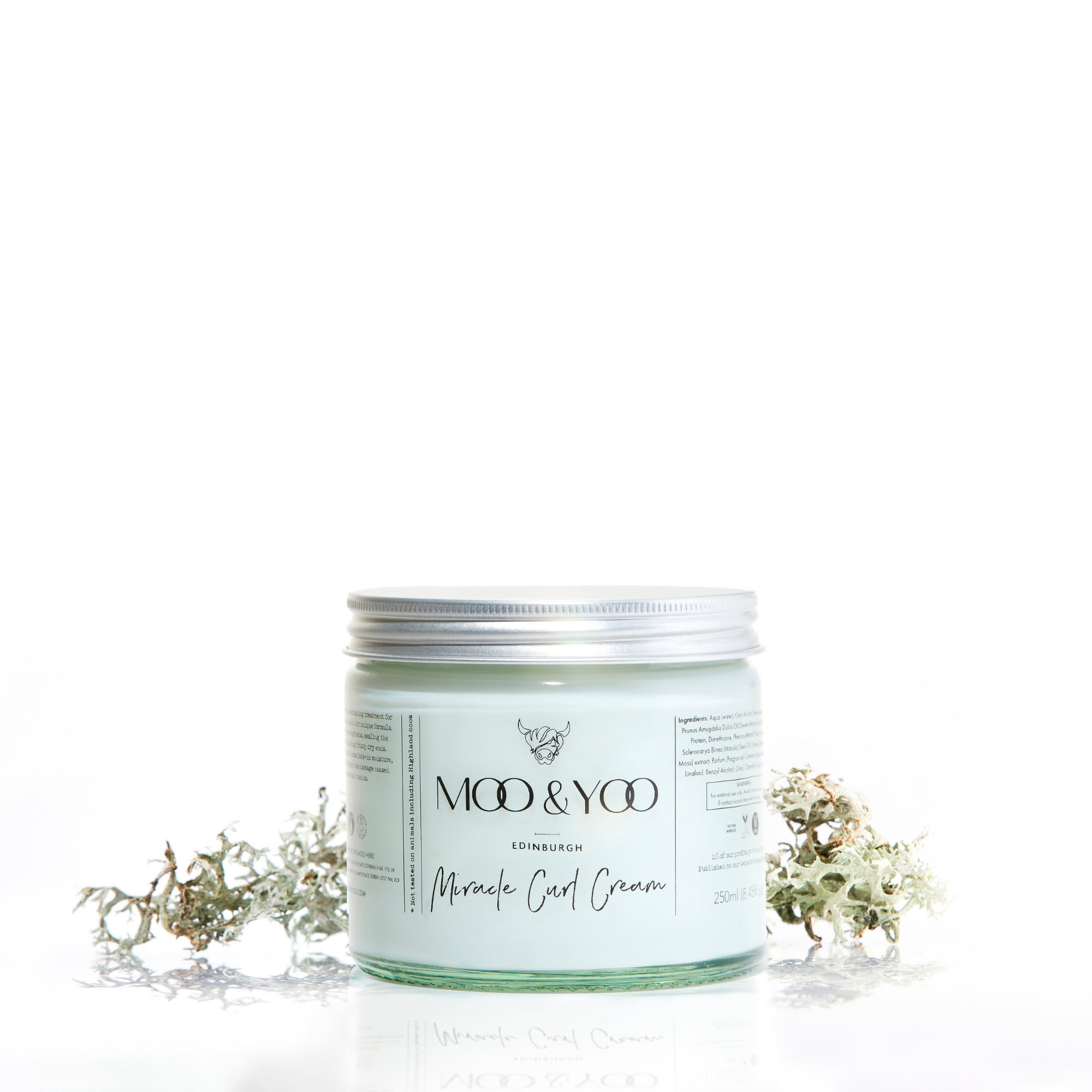 A glass jar of Moo and Yoo Miracle Curl Cream with an aluminium lid on a white background with a sprig of Icelandic moss placed to each side.