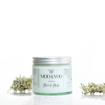 A glass jar of Moo and Yoo Miracle Mask with an aluminium lid on a white background with a sprig of Icelandic moss placed to each side.
