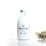 A glass bottle of Moo and Yoo Miracle Milk with an aluminium lid on a white background with a sprig of Icelandic moss placed to one side.