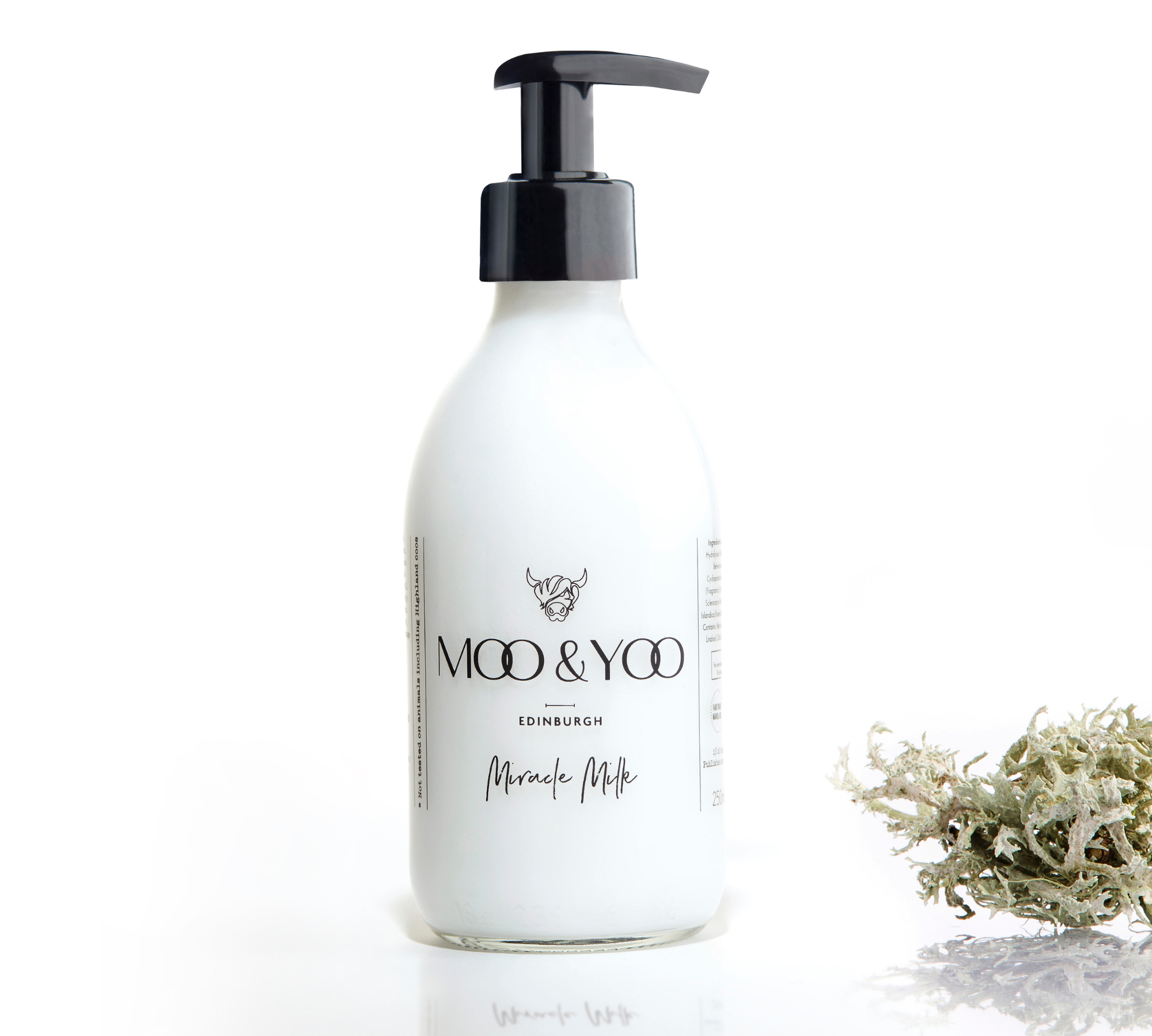 A glass bottle of Moo and Yoo Miracle Milk with a pump on a white background with a sprig of Icelandic moss placed to one side