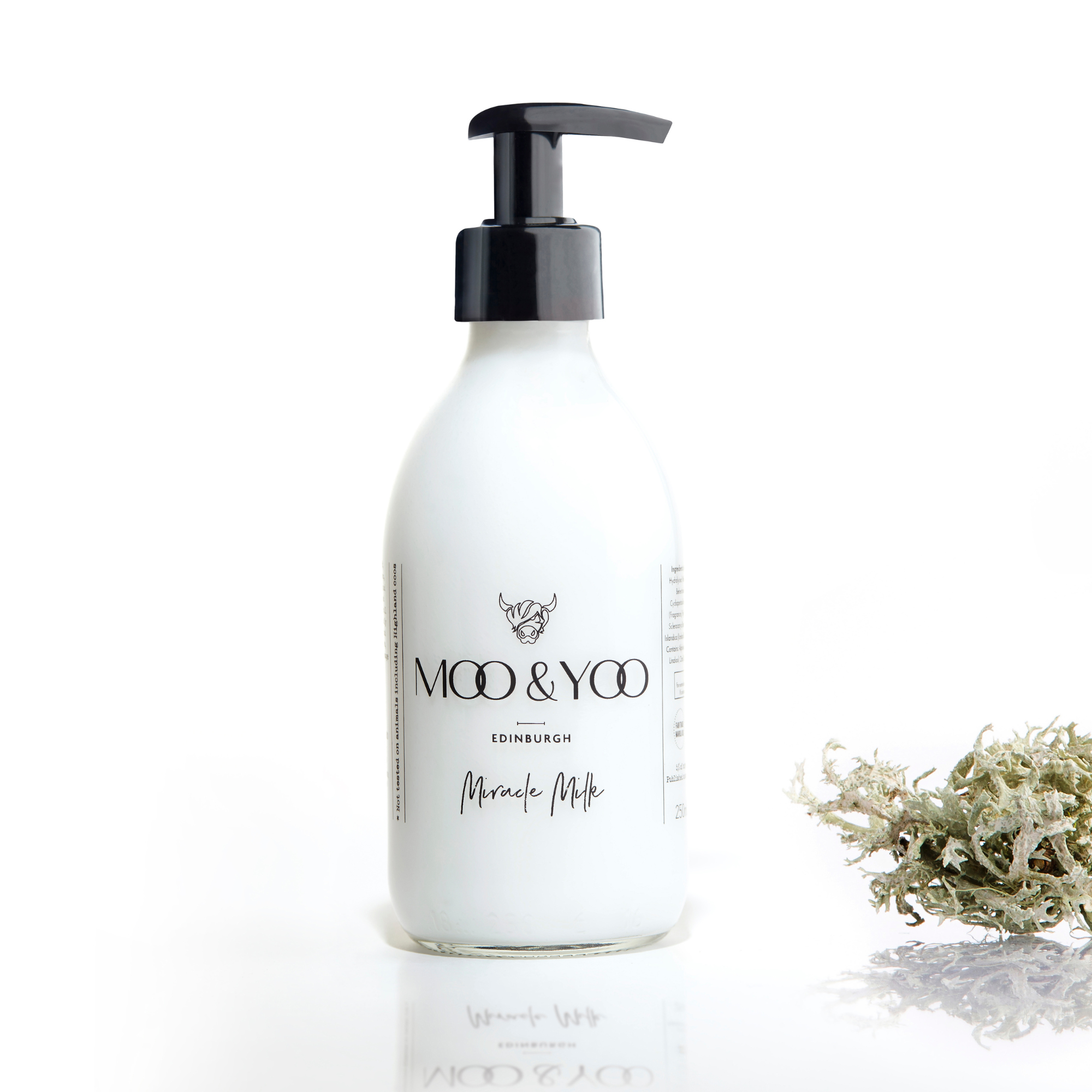 A glass bottle of Moo and Yoo Miracle Milk with a pump on a white background with a sprig of Icelandic moss placed to one side